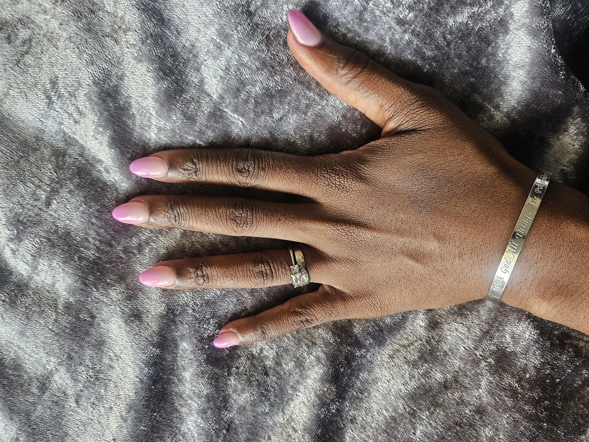 Long pale pink and nude ombre nails, hand resting on a grey fur throw