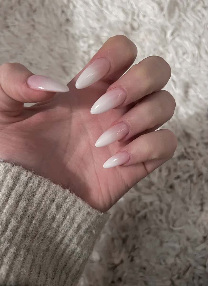 A side-on detail of long white and pink ombre almond nails